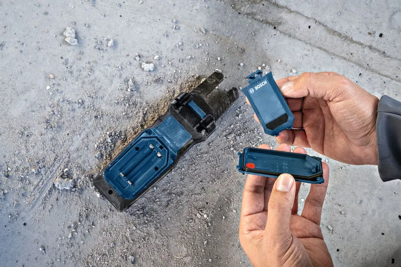 Een persoon vervangt een accu in de houder van een elektrisch gereedschap op een stoffige betonnen vloer.