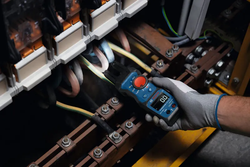 Een persoon die veiligheidsuitrusting draagt, gebruikt een vorkmeter om elektrische draden in een paneel te testen.