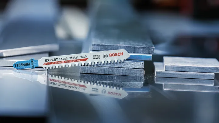 Het decoupeerzaagblad ligt op gestapelde metalen platen op een reflecterend oppervlak.