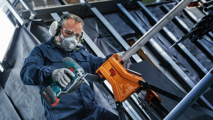 Een persoon die veiligheidsuitrusting draagt, snijdt metalen buizen door met een snoerloos elektrisch gereedschap.