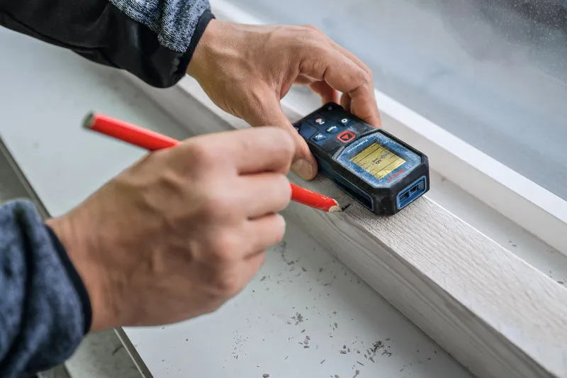 Persoon gebruikt een laserafstandsmeter om een meting op een houten oppervlak te markeren.