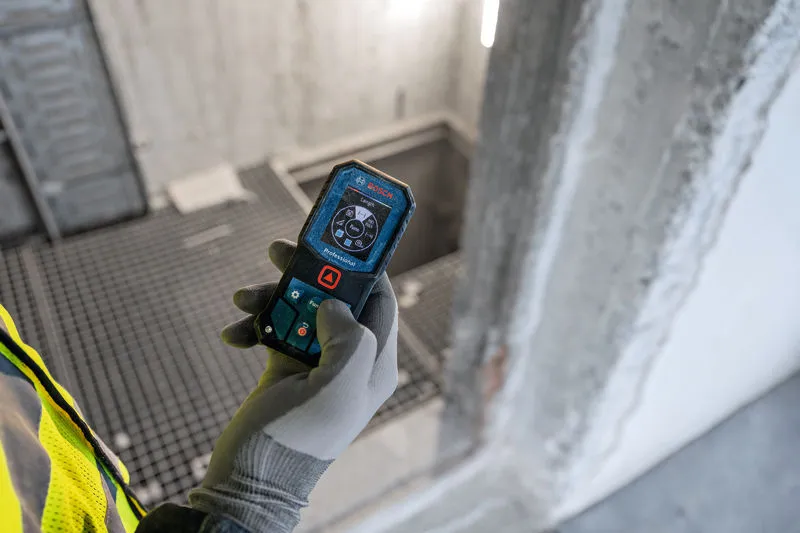 Een persoon die veiligheidsuitrusting draagt, gebruikt een laserafstandsmeter op een bouwplaats.