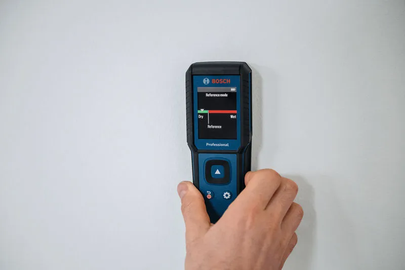 Met een vochtmeter controleert iemand het vochtgehalte van een muur.