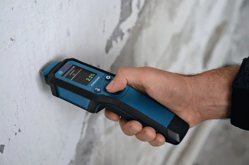 Met een vochtmeter controleert iemand het vochtgehalte in een muur.