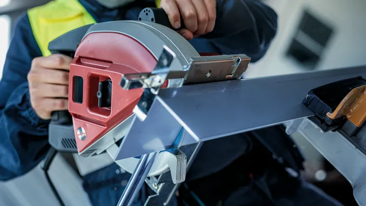 Een persoon die veiligheidsuitrusting draagt, zaagt een metalen balk door met een cirkelzaag.