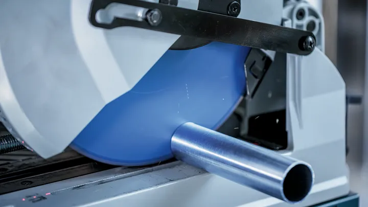 Metalen buis wordt met een cirkelzaag doorgesneden in een industriële omgeving.