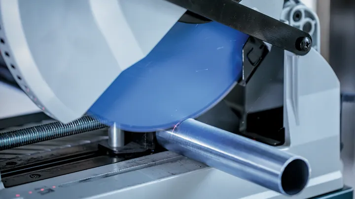 Een metaalzaag snijdt door een ronde metalen pijp, waarbij vonken vrijkomen.