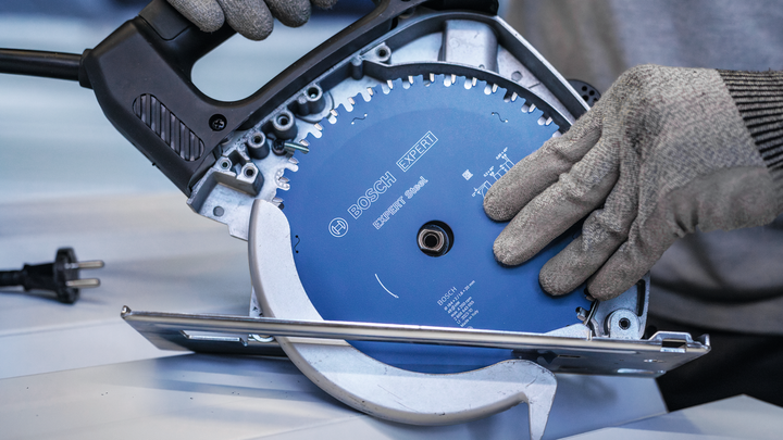 Een persoon die veiligheidsuitrusting draagt, bevestigt een cirkelzaagblad in een elektrisch gereedschap.
