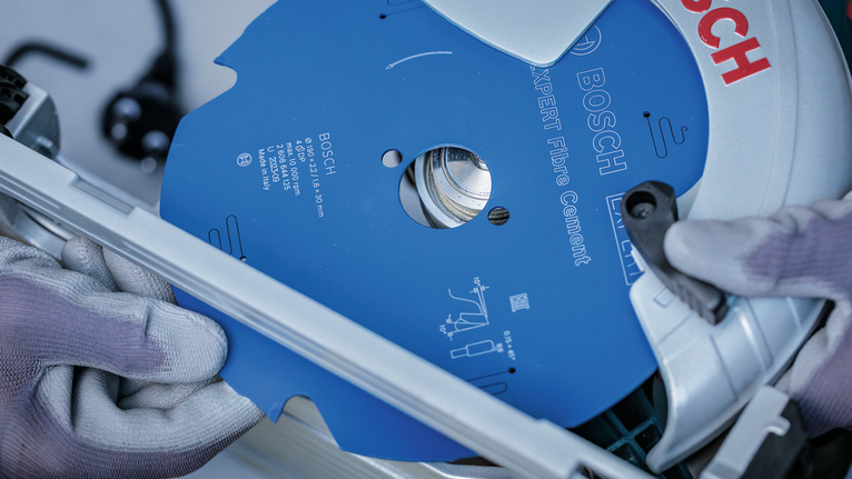 Een persoon die veiligheidsuitrusting draagt, installeert een blauw cirkelzaagblad in een elektrisch gereedschap.