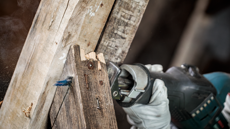 Een persoon die veiligheidsuitrusting draagt, zaagt een houten balk af met een reciprozaag.