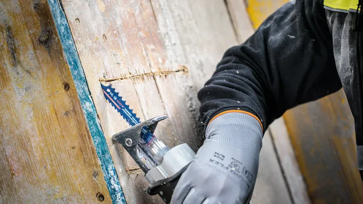 Een persoon met veiligheidsuitrusting zaagt hout met een reciprozaag.
