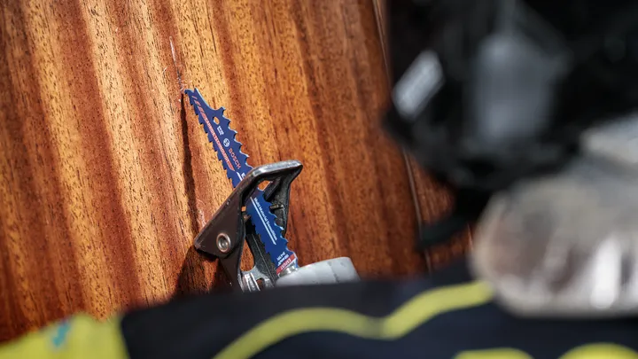 Een persoon die veiligheidsuitrusting draagt, bedient een decoupeerzaag om een houten oppervlak te zagen.