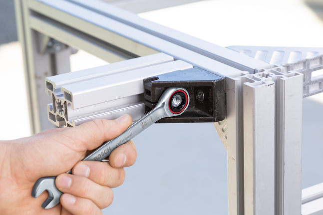 Persoon gebruikt een ratelsleutel om een bout op een aluminium frame vast te draaien.
