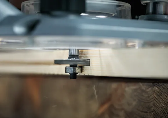 Een freesmachine freest de rand van een houten plank in een houtbewerkingsopstelling.