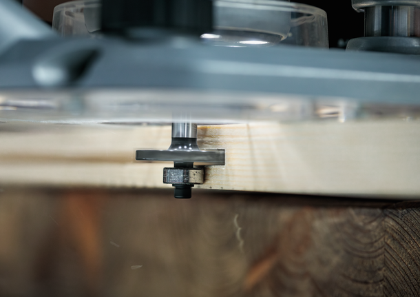 Een freesmachine freest de rand van een houten plank in een houtbewerkingsopstelling.
