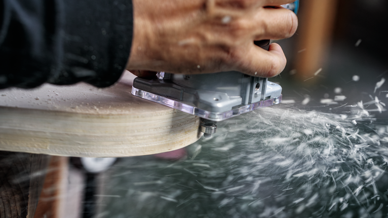 Een persoon beweegt een elektrisch gereedschap langs de rand van het hout, terwijl de houtkrullen rondvliegen.