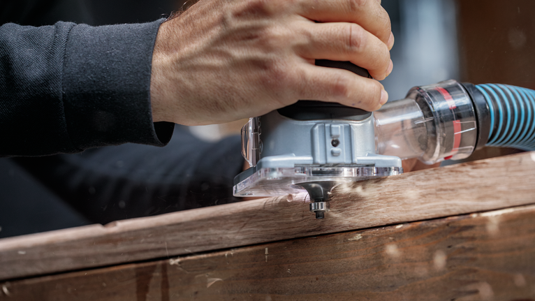 Persoon gebruikt een bovenfreesmachine langs een houten plank om nauwkeurig randen te vormen.