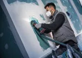 Een persoon die veiligheidsuitrusting draagt, gebruikt een snoerloze multi-cutter om gipsplaat te snijden.