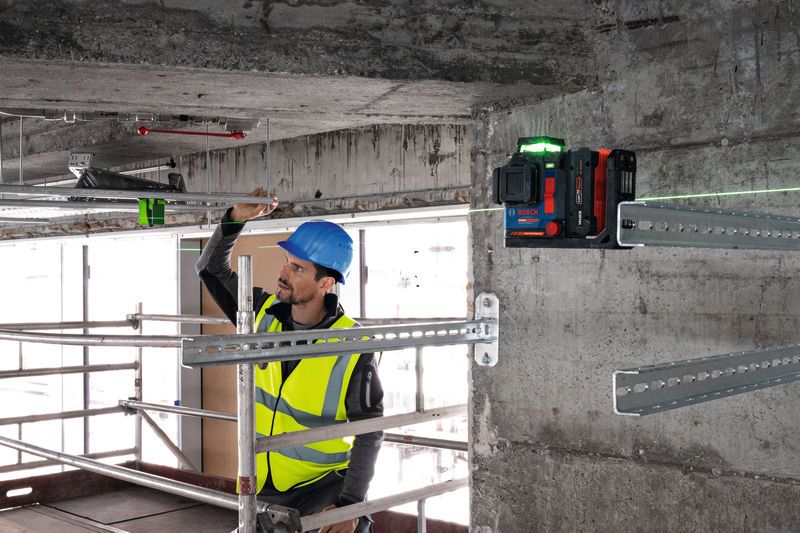 Een persoon die veiligheidsuitrusting draagt, lijnt metalen rails uit met behulp van een laserwaterpasinstrument.