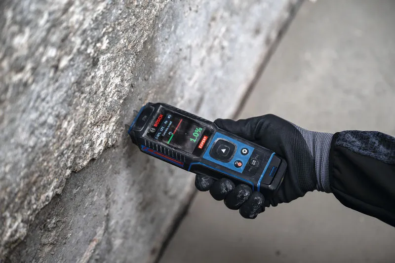 Een persoon die veiligheidsuitrusting draagt, gebruikt een vochtmeter voor materialen op een betonnen muur.