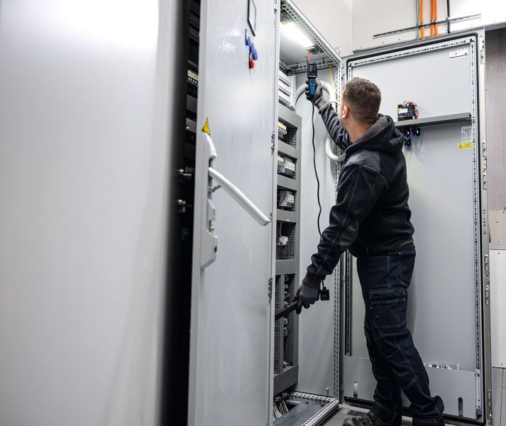 Een persoon die veiligheidsuitrusting draagt, test een elektrisch paneel met een spanningszoeker.