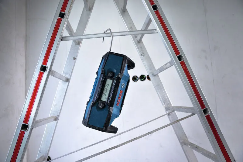 Bouwradio hangt aan een metalen haak aan een ladder op een bouwterrein.