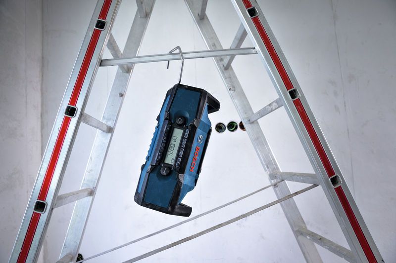 Bouwradio hangt aan een metalen haak aan een ladder op een bouwterrein.