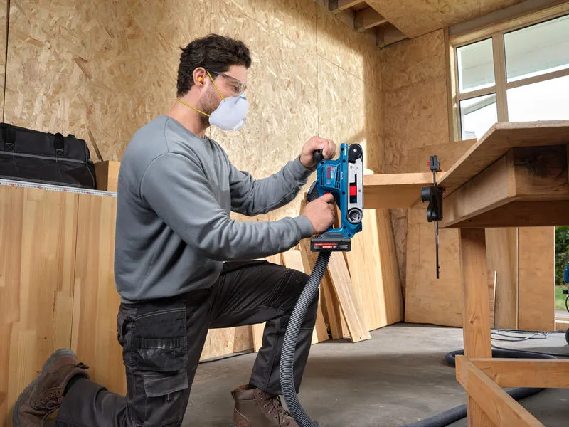 Een persoon die veiligheidsuitrusting draagt, gebruikt een bandschuurmachine op een houten plank.