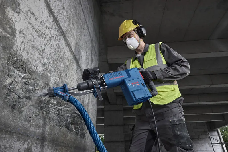 Een persoon die veiligheidsuitrusting draagt, gebruikt een sloophamer om beton te breken.
