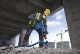 Een persoon met veiligheidsuitrusting sloopt beton met een sloophamer.
