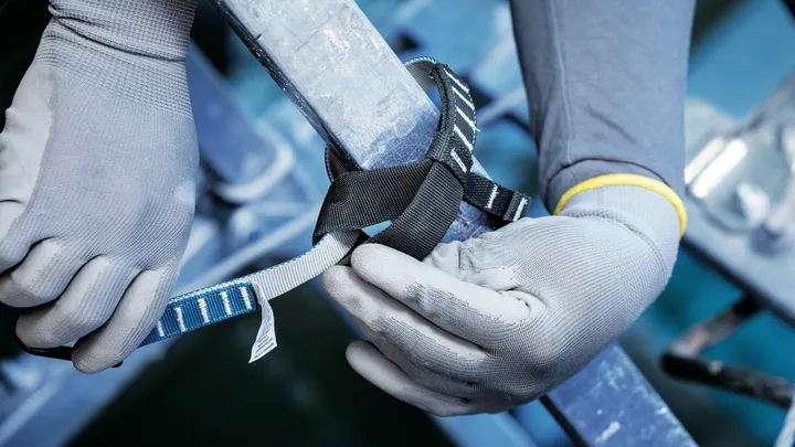 Een persoon die veiligheidsmateriaal draagt, bevestigt een veiligheidsriem rond een metalen leuning.