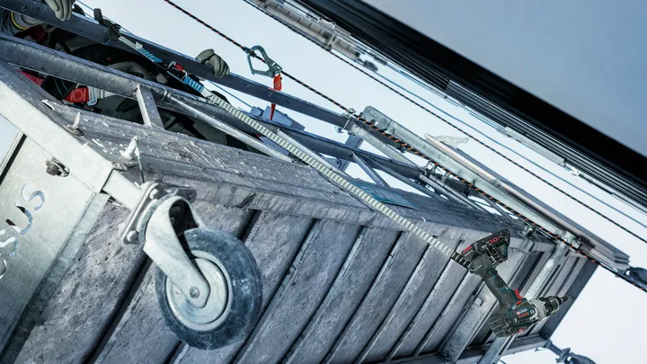 Een persoon die veiligheidsuitrusting draagt, gebruikt een boormachine op een metalen constructie.