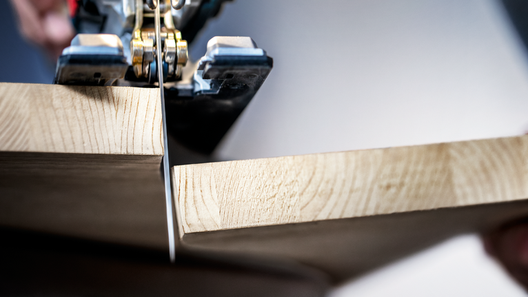 Iemand zaagt een houten plank met een decoupeerzaag.