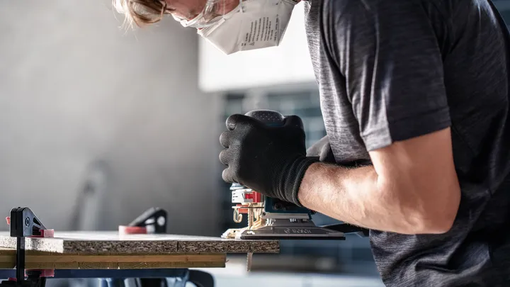 Een persoon die veiligheidsuitrusting draagt, gebruikt een elektrisch gereedschap om hout te zagen.