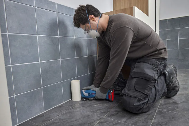 Een persoon die veiligheidsuitrusting draagt, gebruikt een multifunctioneel gereedschap om vloertegels te snijden.