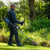 Een persoon die veiligheidsuitrusting draagt, maait het gras bij een tuin met een bosmaaier.