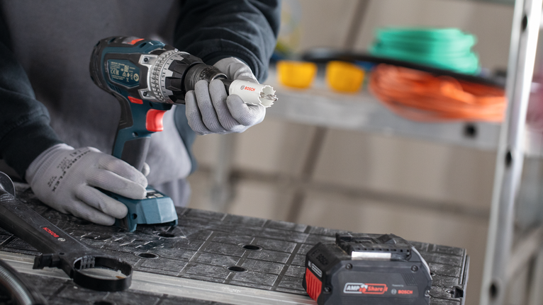 Een persoon die veiligheidsuitrusting draagt, bevestigt een gatenzaag aan een accuboormachine.