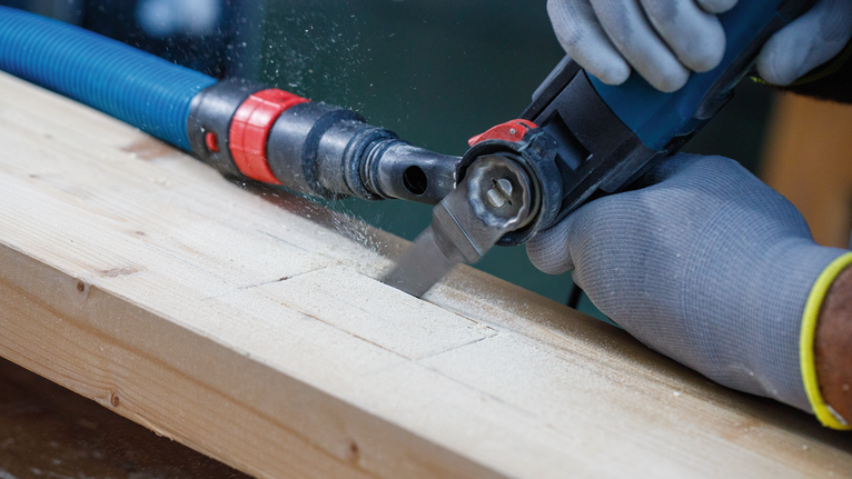 Een persoon met veiligheidsuitrusting zaagt een houten plank met een elektrisch gereedschap.