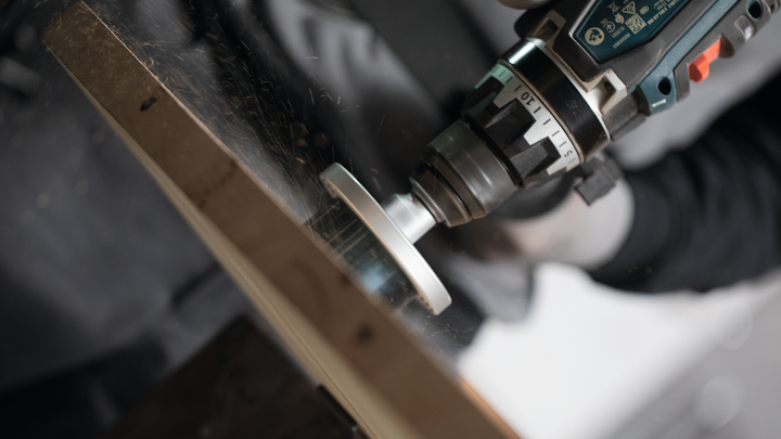 Persoon gebruikt een boormachine om een metalen rand te slijpen, draagt veiligheidsuitrusting.