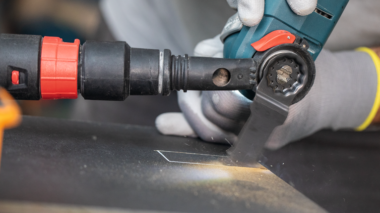 Een persoon die veiligheidsuitrusting draagt, gebruikt een elektrisch gereedschap om een nauwkeurige rechthoek in een metalen plaat te snijden.