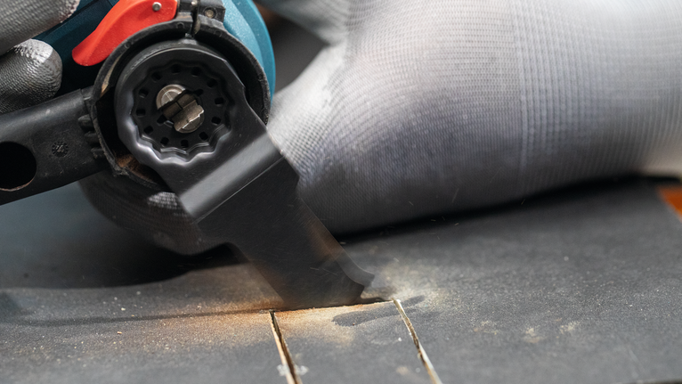 Een persoon die veiligheidsuitrusting draagt, gebruikt een elektrisch gereedschap om een groef in hout te maken.