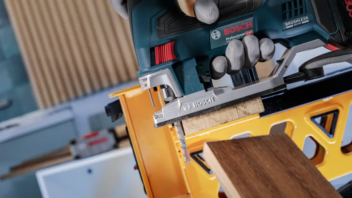 Een persoon die veiligheidsuitrusting draagt, gebruikt een decoupeerzaag om hout te zagen op een werkbank.