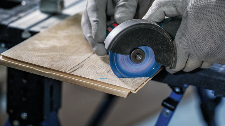 Een persoon met veiligheidsuitrusting zaagt een houten plank met een haakse slijper.