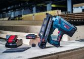 Draadloze tacker met accu's en oplader, geplaatst op een werkbank op een bouwplaats.