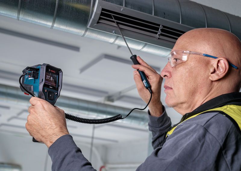 Een persoon met veiligheidsuitrusting inspecteert een luchtkanaal met een draagbare inspectiecamera.