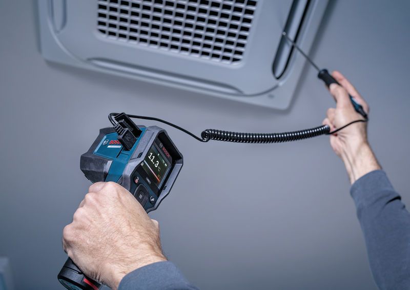 Iemand meet de luchttemperatuur bij een plafondventilator met behulp van een digitaal inspectie-instrument.