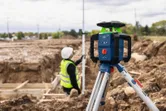 Laserwaterpas op statief op een bouwplaats met een persoon die veiligheidsuitrusting draagt.