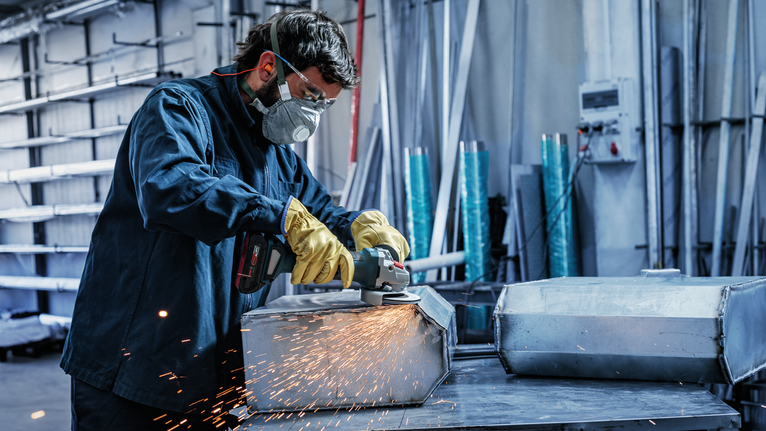 Een persoon met veiligheidsuitrusting slijpt een metalen doos met een haakse slijper.