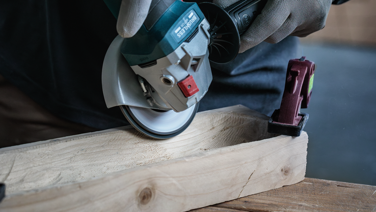 Een persoon met veiligheidsuitrusting zaagt een houten plank door met een haakse slijper.
