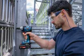 Een persoon die veiligheidsuitrusting draagt, gebruikt een snoerloze slagmoersleutel op een metalen constructie.